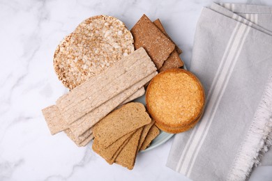 Photo of Rye crispbreads, rice cakes and rusks on white marble table, flat lay