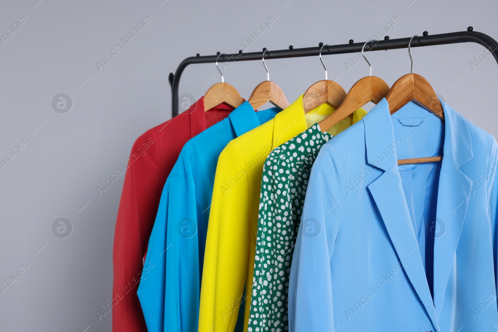 Photo of Rack with stylish women`s clothes on wooden hangers against light grey background, space for text