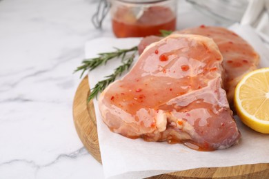 Photo of Board with raw marinated meat, lemon and rosemary on white marble table, closeup. Space for text