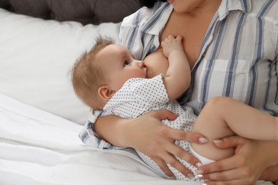 Woman breastfeeding her little baby on bed indoors