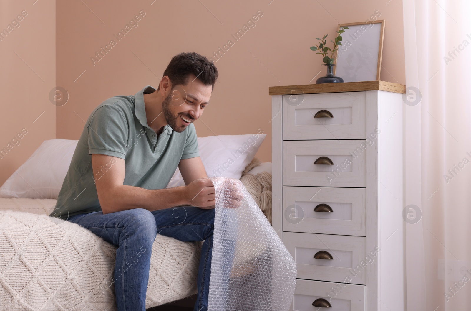 Photo of Man popping bubble wrap in bedroom at home. Stress relief