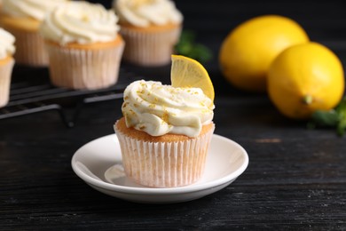 Photo of Delicious cupcakes with white cream, lemon zest and lemons on black wooden table, closeup