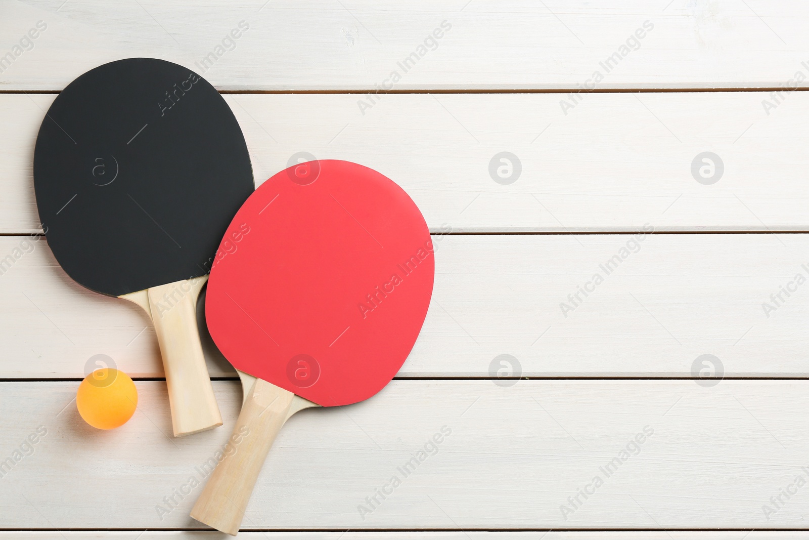 Photo of Ping pong rackets and ball on white wooden table, flat lay. Space for text