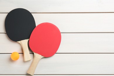 Photo of Ping pong rackets and ball on white wooden table, flat lay. Space for text