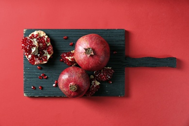 Wooden board with ripe pomegranates on color background, top view