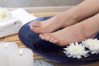 Photo of Woman soaking her feet in bowl with water and flowers on floor, closeup. Spa treatment