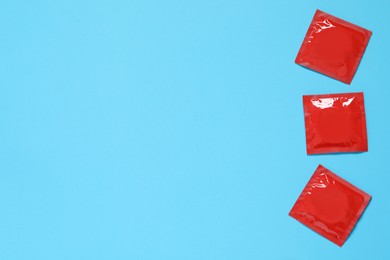 Photo of Condom packages on light blue background, flat lay and space for text. Safe sex