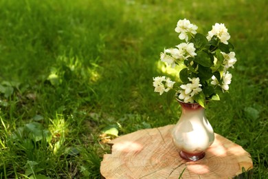 Bouquet of beautiful jasmine flowers in vase on wooden stump outdoors, space for text