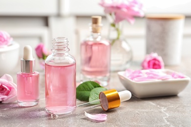 Photo of Bottles of rose essential oil, pipette and flowers on table, space for text