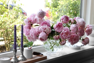 Beautiful pink peonies in vase and tray with candles on window sill. Interior design