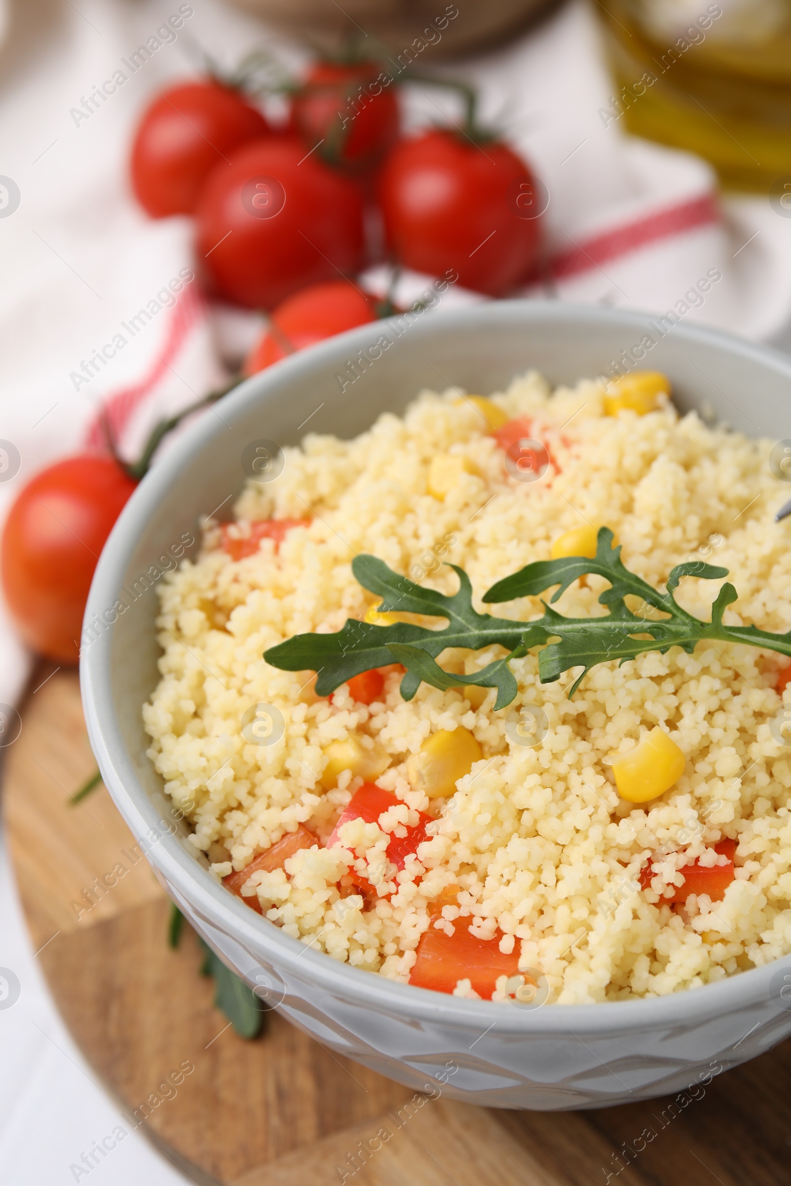 Photo of Tasty couscous with pepper, corn and arugula in bowl on white table, closeup