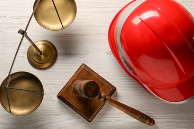 Photo of Law concept. Gavel, scales and red hard hat on white wooden table, flat lay