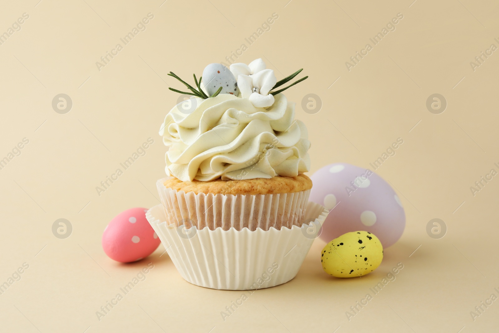 Photo of Tasty Easter cupcake with vanilla cream and candies on beige background