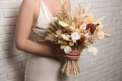 Photo of Bride holding beautiful dried flower bouquet near white brick wall, closeup