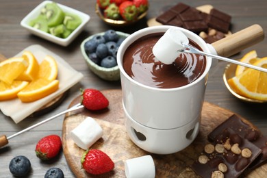 Dipping sweet marshmallow in fondue pot with melted chocolate at wooden table