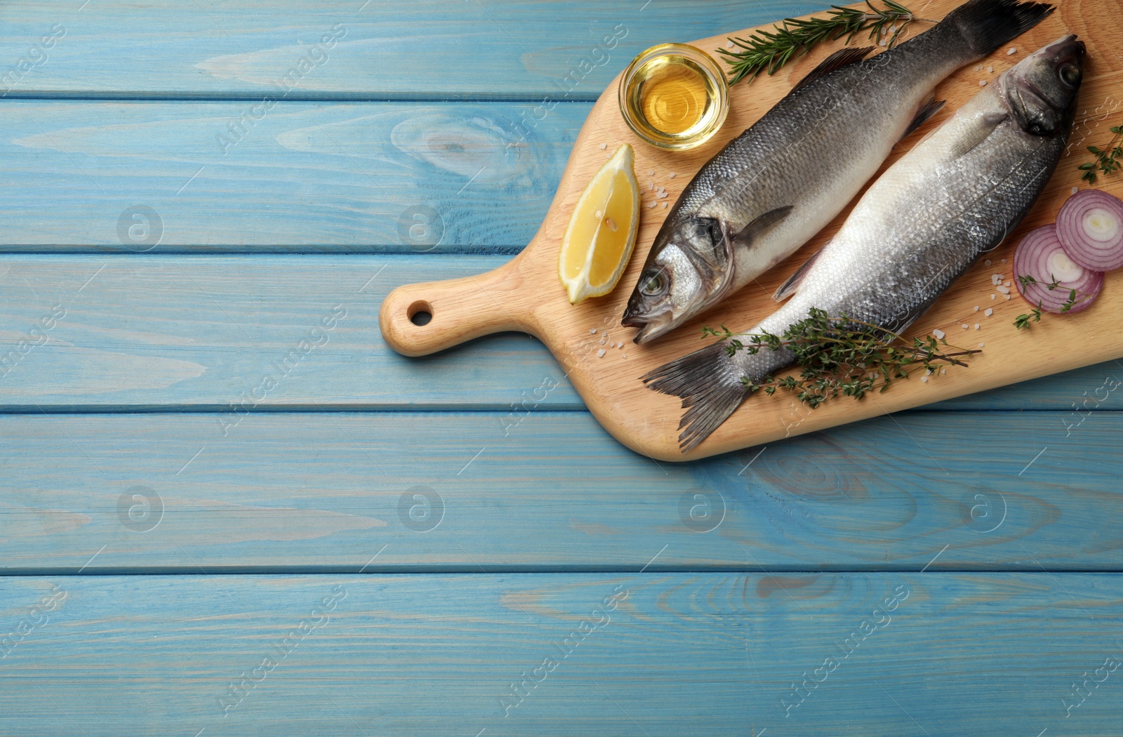 Photo of Sea bass fish and ingredients on light blue wooden table, top view. Space for text