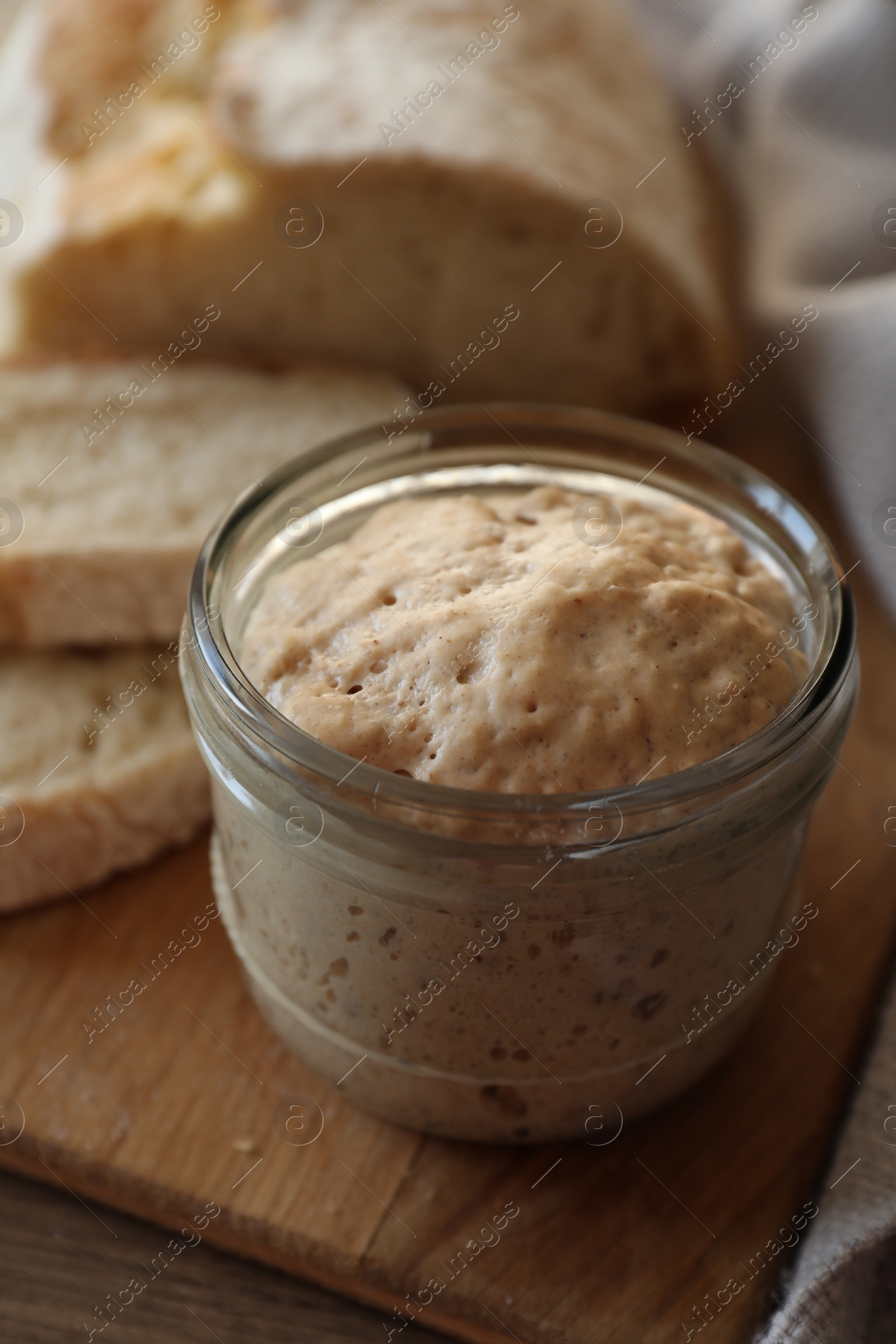 Photo of Sourdough starter in glass jar and bread on table, closeup