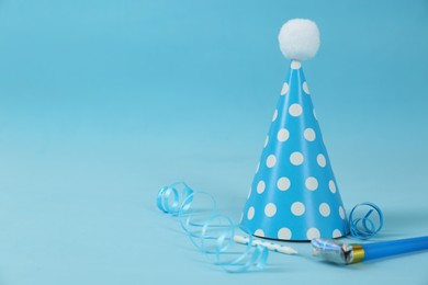 Bright party hat, horn, candle and serpentine streamers on light blue background. Space for text