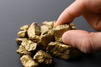 Photo of Man taking gold nugget from pile on dark background, closeup