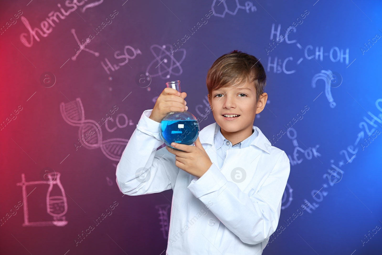 Photo of Schoolboy holding Florence flask against blackboard with written chemistry formulas