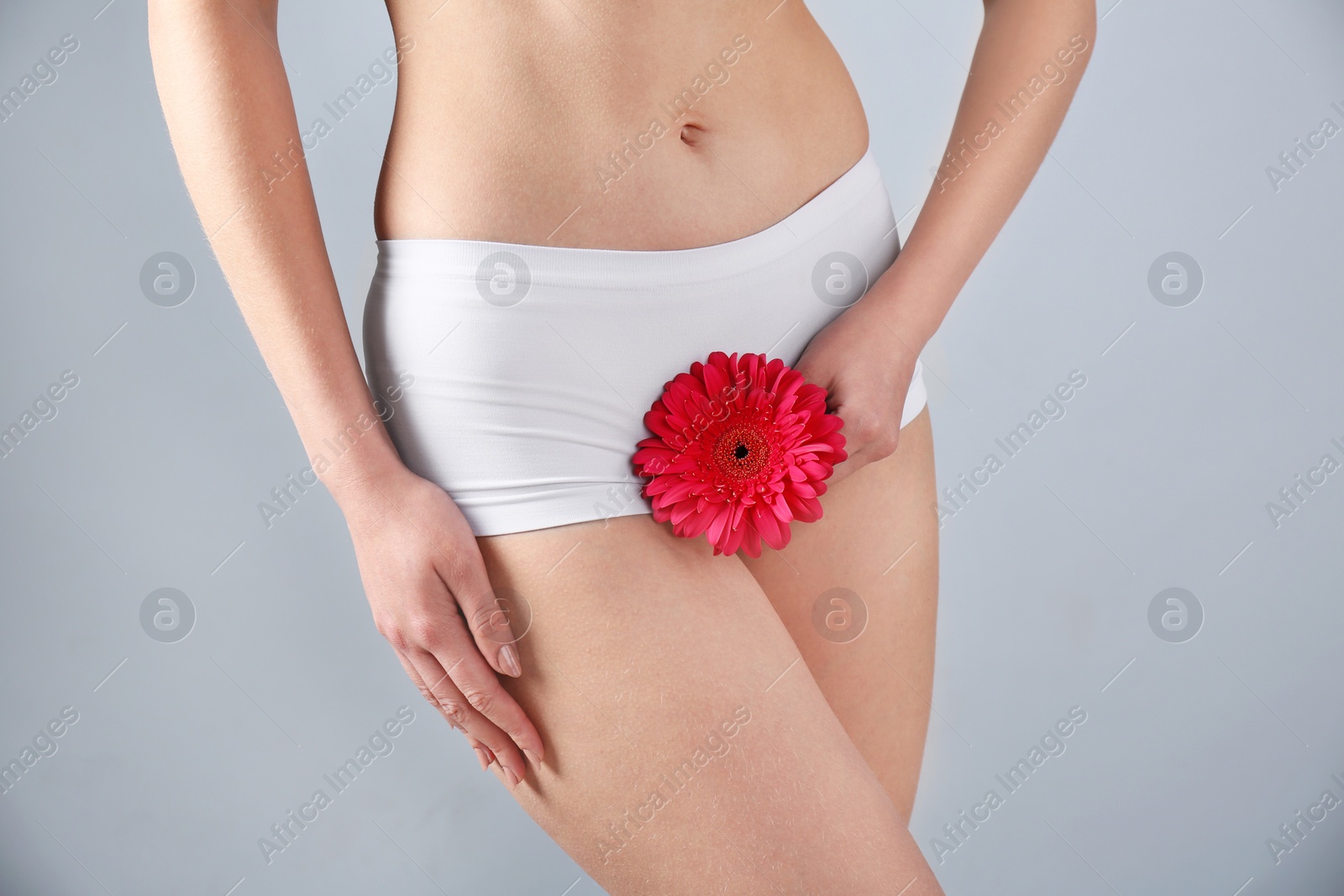 Photo of Young woman holding flower near underwear on grey background. Gynecology