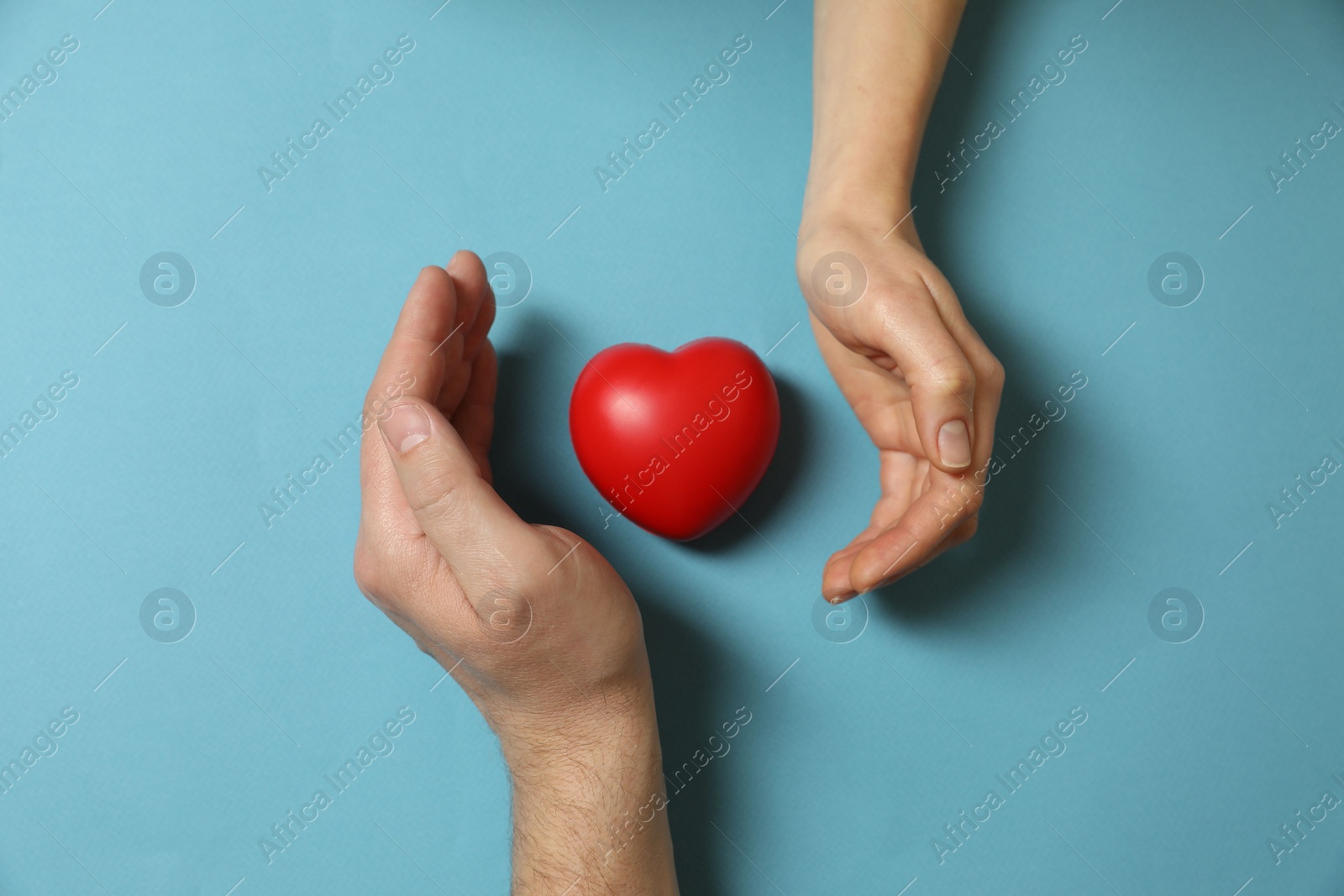 Photo of Couple protecting red decorative heart on light blue background, top view