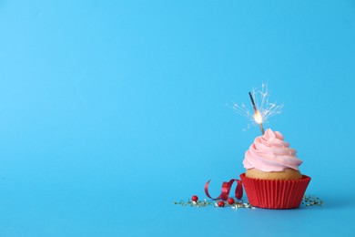 Photo of Birthday cupcake with burning sparkler on light blue background. Space for text