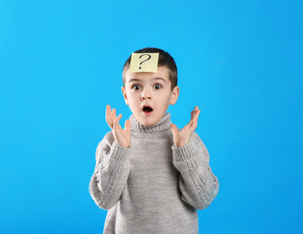 Photo of Emotional little boy with question mark on light blue background