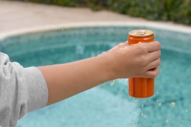 Photo of Woman holding tasty open canned beverage near swimming pool, closeup