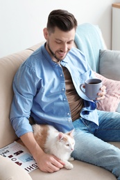 Young man with cute cat on sofa at home