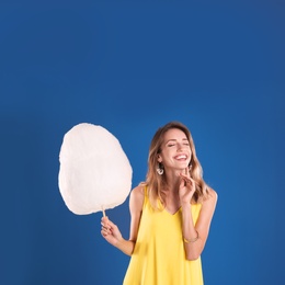 Happy young woman with cotton candy on blue background