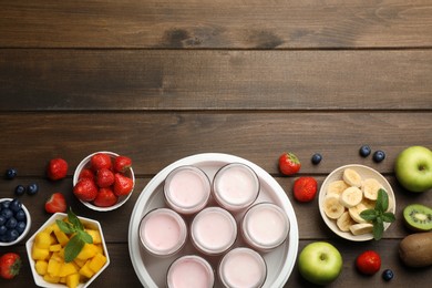 Modern yogurt maker with full jars and different fruits on wooden table, flat lay. Space for text