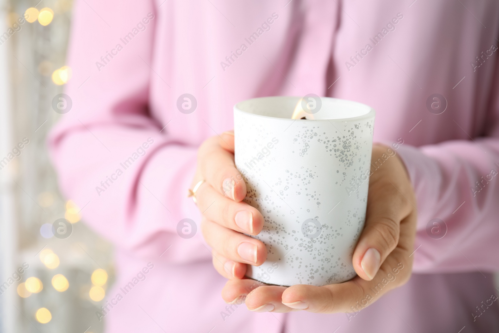 Photo of Woman holding burning candle with wooden wick against festive lights, closeup