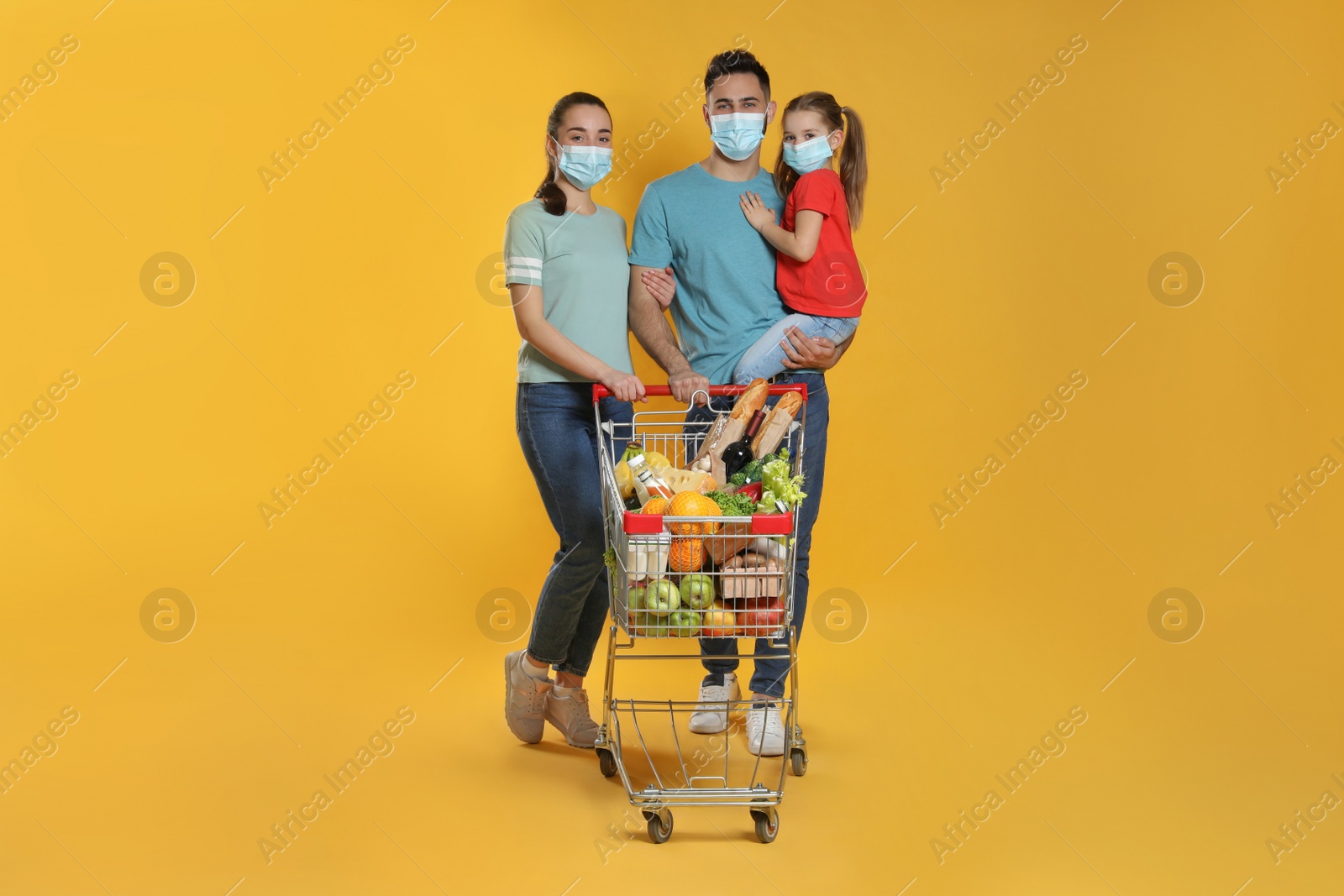 Photo of Family with protective masks and shopping cart full of groceries on yellow background