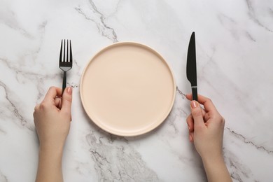 Photo of Woman with empty plate and cutlery at white marble table, top view
