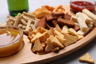 Photo of Wooden tray with different crispy rusks and dip sauces on table, closeup