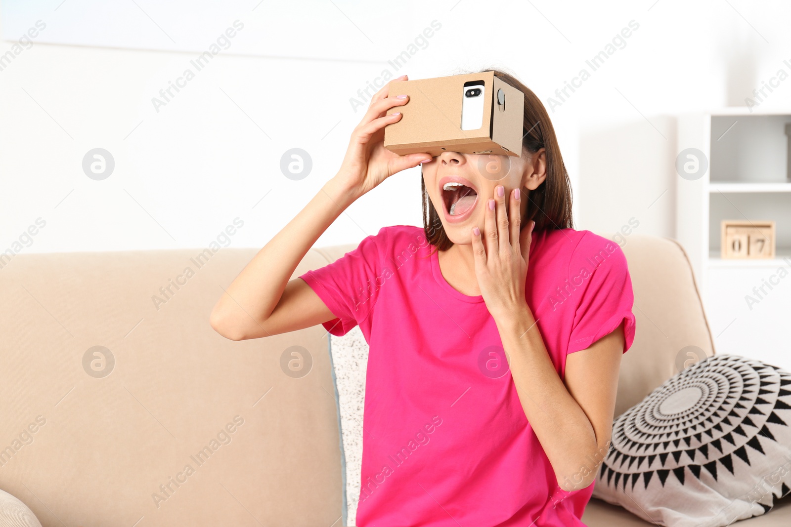 Photo of Young woman using cardboard virtual reality headset at home