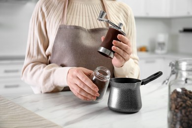 Photo of Woman opening coffee grinder at table indoors, closeup