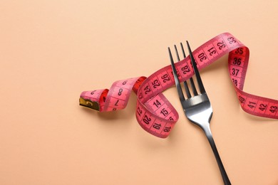 Photo of Fork with measuring tape on pale orange background, top view with space for text. Diet concept