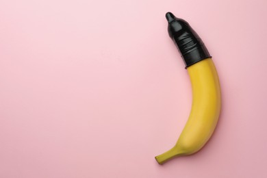 Photo of Banana with condom on pink background, top view and space for text. Safe sex concept