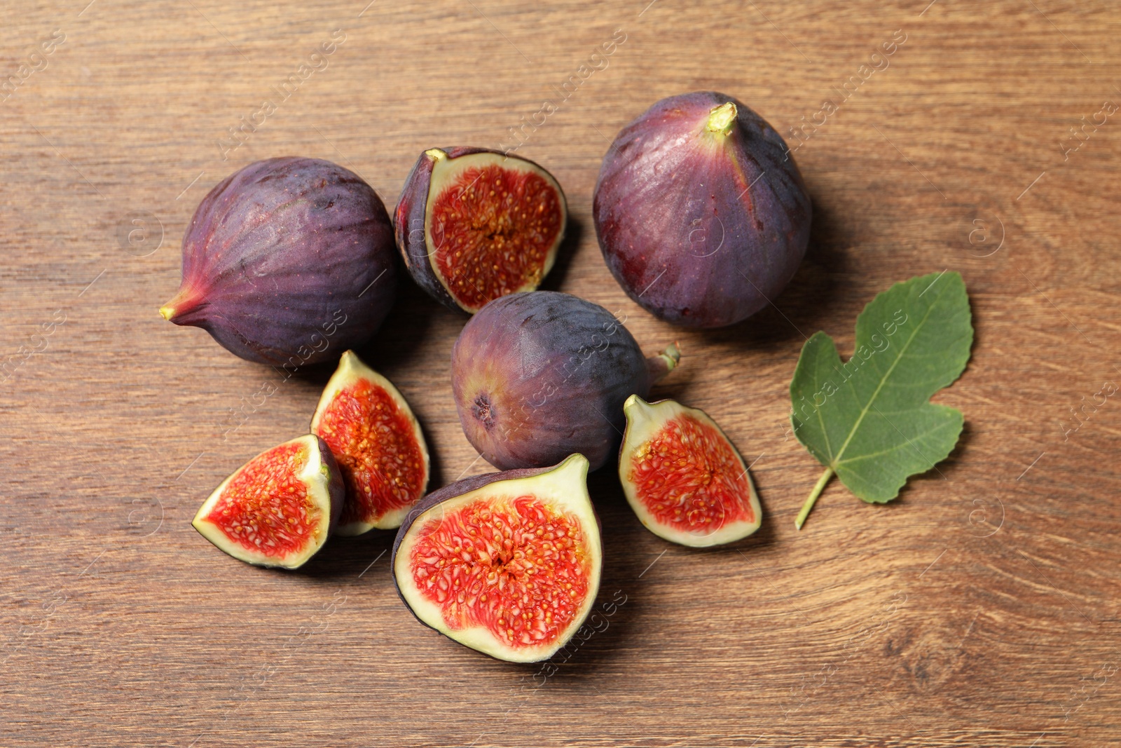 Photo of Whole and cut ripe figs with leaf on wooden table, flat lay