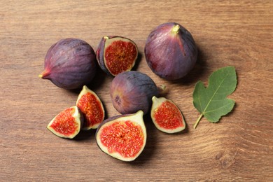 Whole and cut ripe figs with leaf on wooden table, flat lay