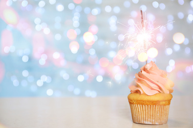 Image of Birthday cupcake with sparkler on table against blurred background. Space for text