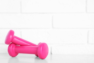 Photo of Stylish dumbbells on table against brick wall, space for text. Home fitness