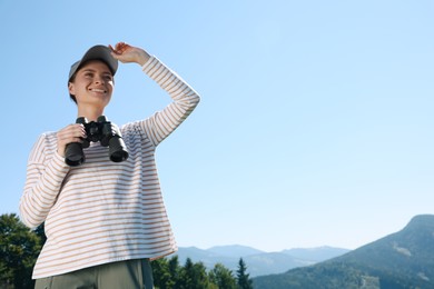 Woman with binoculars in mountains on sunny day, low angle view