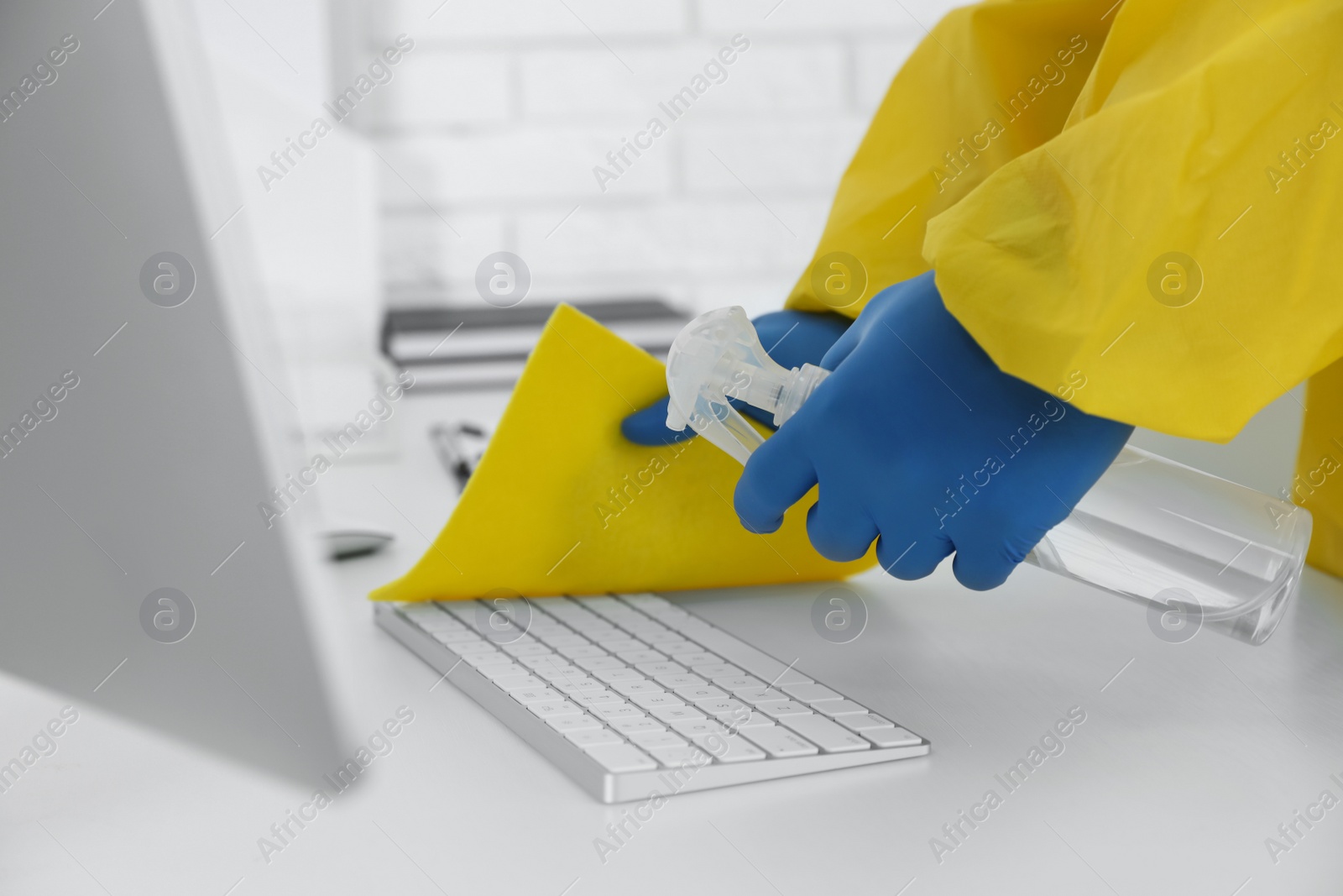 Photo of Employee in protective suit and gloves sanitizing keyboard indoors, closeup. Medical disinfection