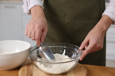 Making bread. Man putting flour into bowl at wooden table in kitchen, closeup