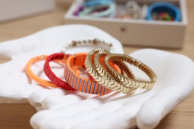 Photo of Ceramic hand stand with many different bracelets on table, closeup