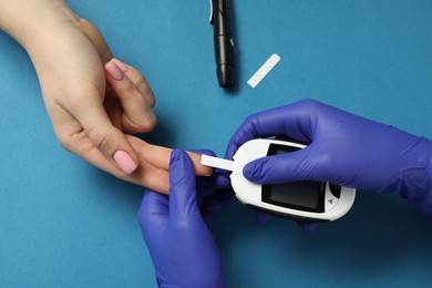 Diabetes. Doctor checking patient's blood sugar level with glucometer on blue background, top view