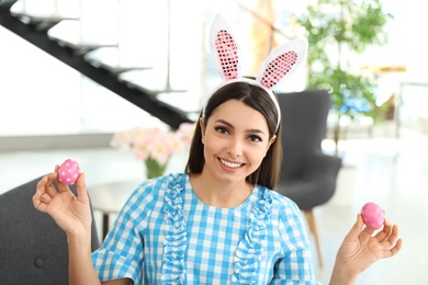Photo of Beautiful woman in bunny ears headband holding Easter eggs at home